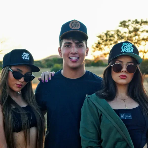 Três amigos usando bonés pretos com logo turquesa personalizada em um campo ao pôr do sol